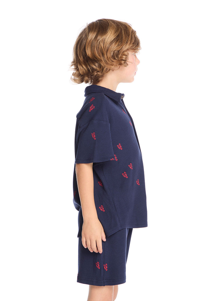 Side view of boy wearing the Chaser Kids Collared Avalon Lobsters Shirt showing short sleeves, button-front design, and relaxed fit, styled with matching shorts and navy sneakers on a white background