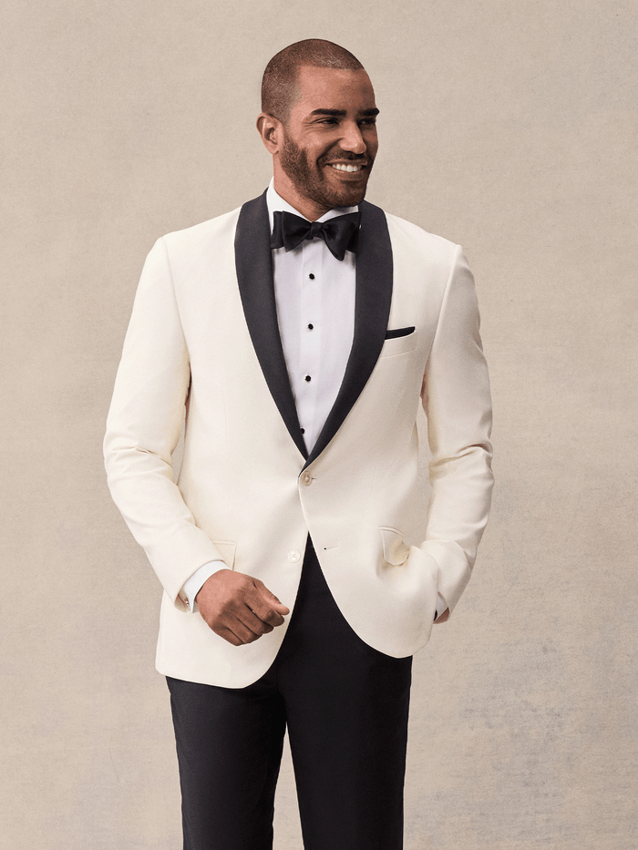 Man in an ivory shawl-lapel tuxedo jacket with black satin lapels, black bow tie, and black trousers.