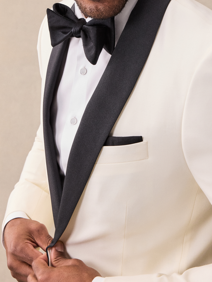 Close-up of black satin shawl lapel, bow tie, and buttons on an ivory tuxedo jacket.