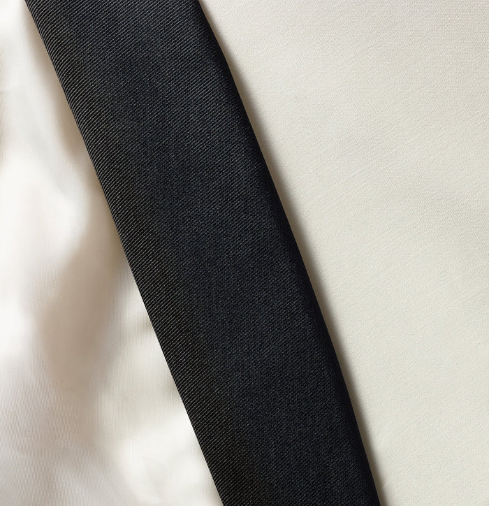 Close-up of black satin lapel edge against ivory tuxedo jacket fabric.