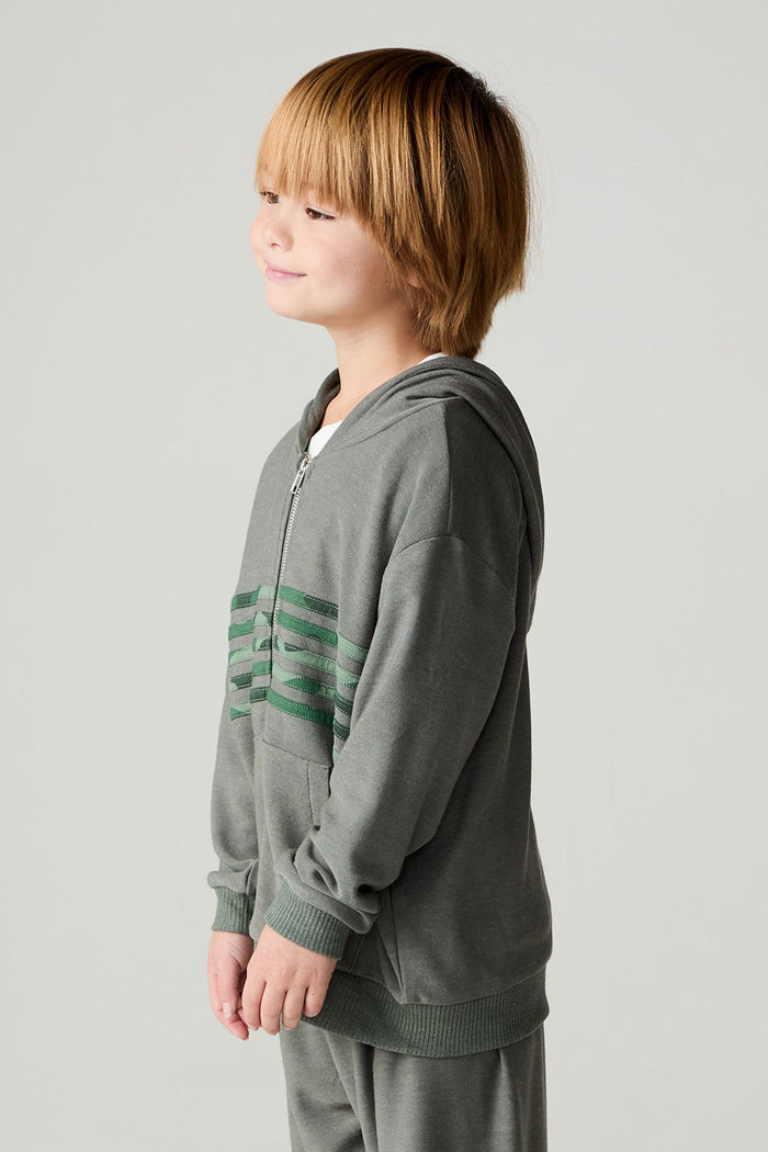 Side view of a boy wearing the Chaser Cool Camo Boys Zip Up on a neutral background and matching pants