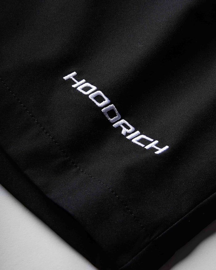 Close-up of a black athletic garment, likely shorts, featuring the brand name 'HOODRICH' embroidered in white with a silver outline on the side.