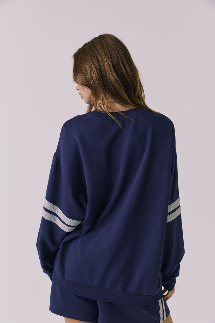 Back view of a woman wearing Chaser's navy blue Cornell Sapphire & Heather Grey Pullover with grey stripes on a plain background