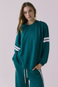 Front view of a woman wearing Chaser's Cornell Pullover in Teal and White with striped sleeves on a plain studio background