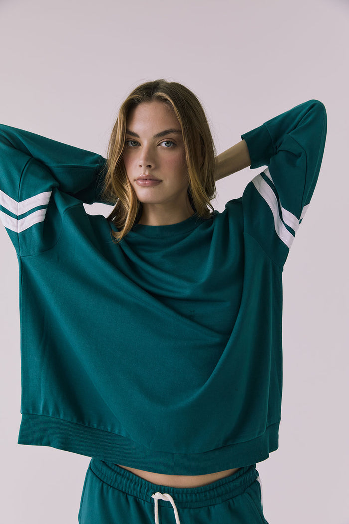 Front view of a woman with her arms up wearing Chaser's Cornell Pullover in Teal and White with striped sleeves on a plain studio background