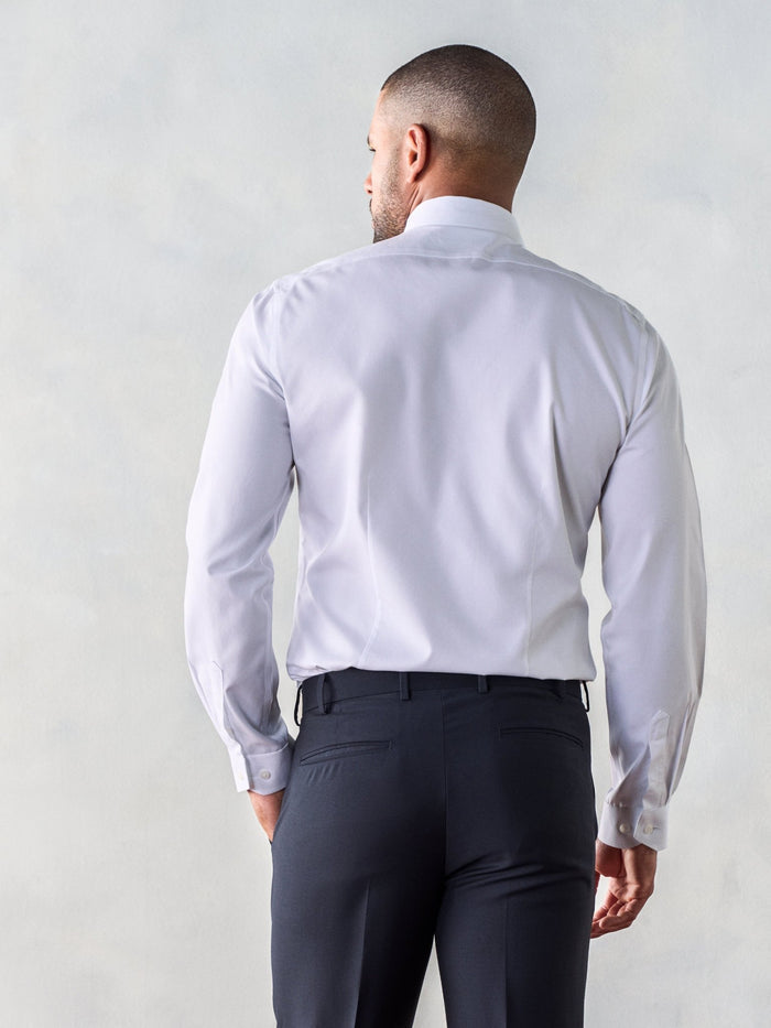 Back view of a man in a white dress shirt and dark trousers, hand in pocket.