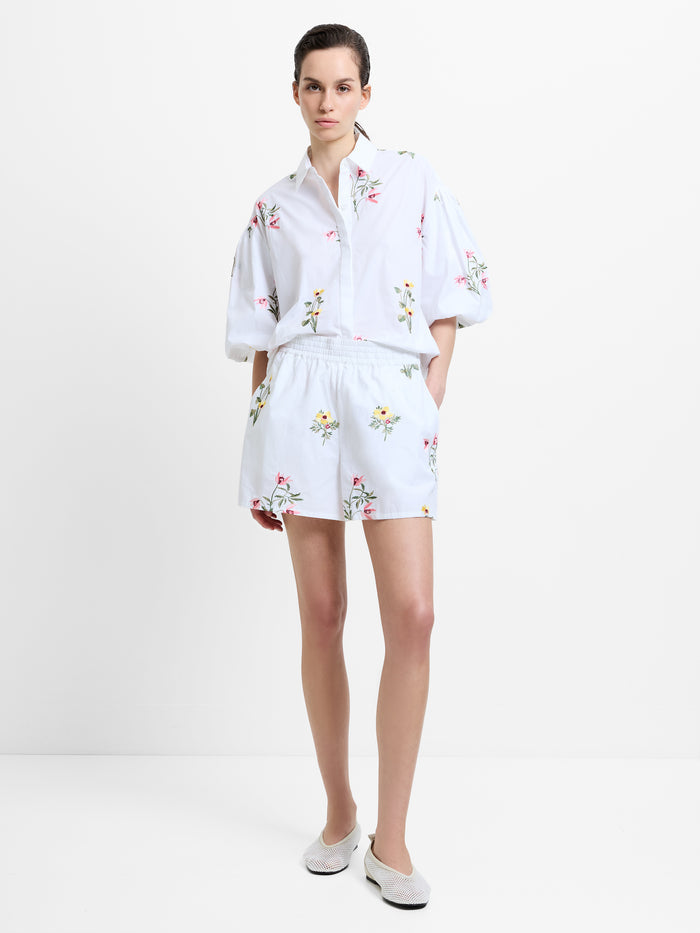 Woman wearing a white short sleeve shirt with floral embroidered details with matching shorts