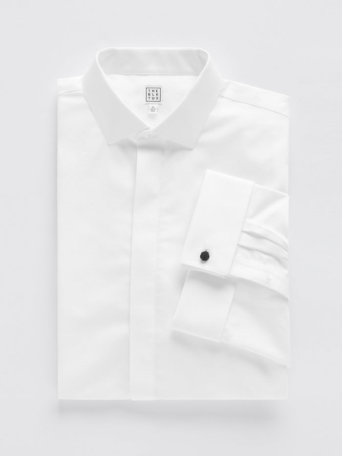 White fly-front tuxedo shirt folded flat, showing covered placket and black cufflink.