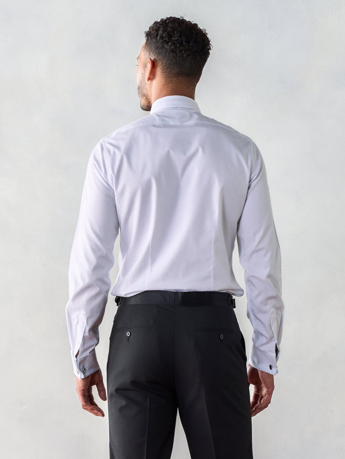 Back view of a man in a white fly-front tuxedo shirt and black trousers.