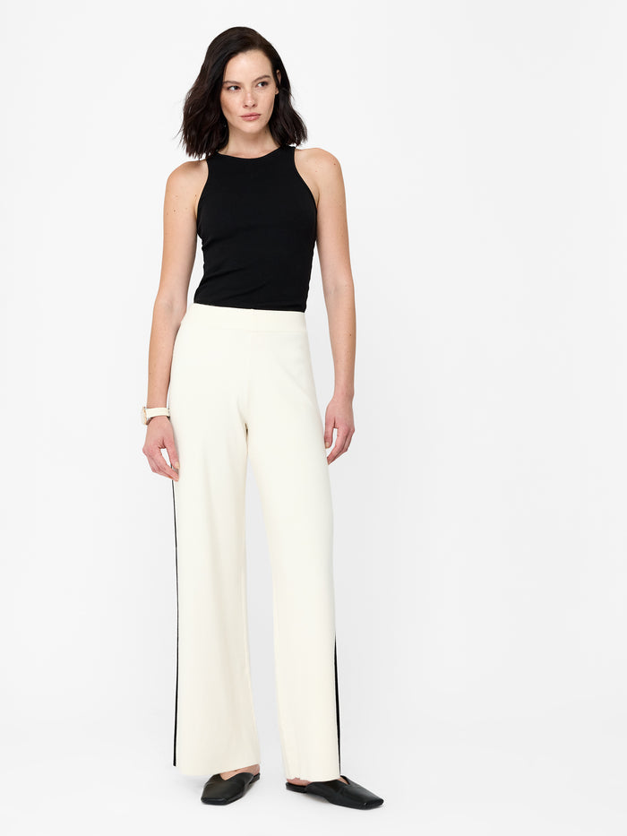A woman wearing a smith knit cream wide leg trousers with an elasticated waistband, a black contrast trim and a full length.