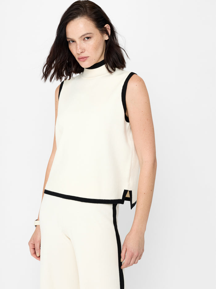A woman wearing a cream high neck vest with short sleeves, a relaxed fit and a black contrast trim.