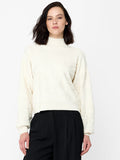 A woman wearing a cream knit Jumper with a floral pattern, long balloon sleeves and a ribbed mock neckline.