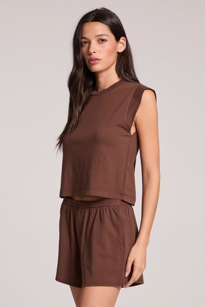 Side angle view of a woman wearing the Chaser  Cropped Cap Sleeve Kahlua Crewneck Tee on a neutral background with arms at her side