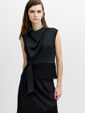 A woman wearing a black sleeveless blouse featuring a draped neckline, lace trimmed hem and a tie front detail.