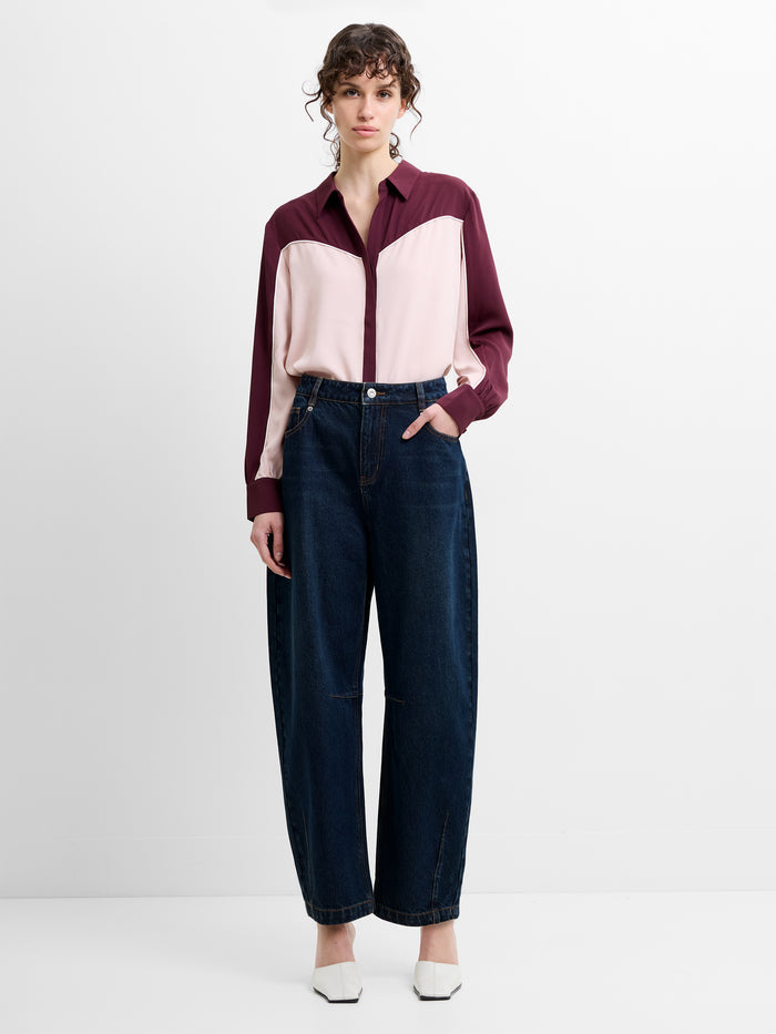 Woman wearing a pink and burgundy shirt with high waisted dark blue balloon leg jeans