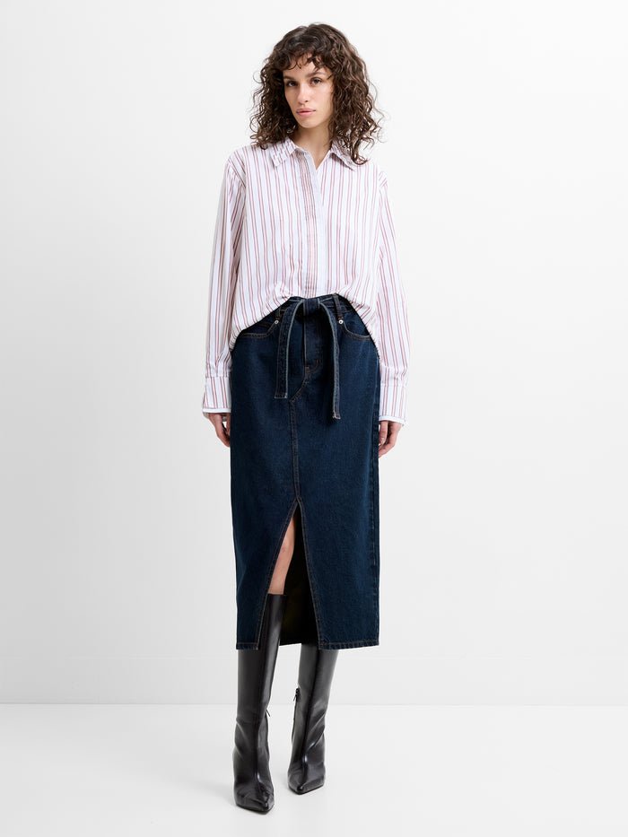 Woman wearing a high waisted, dark blue denim mid skirt with a self tie belted waist and a front slit