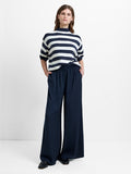 Woman wearing a short sleeve white and navy jumper with wide leg, high waisted elasticated trousers with two side pockets