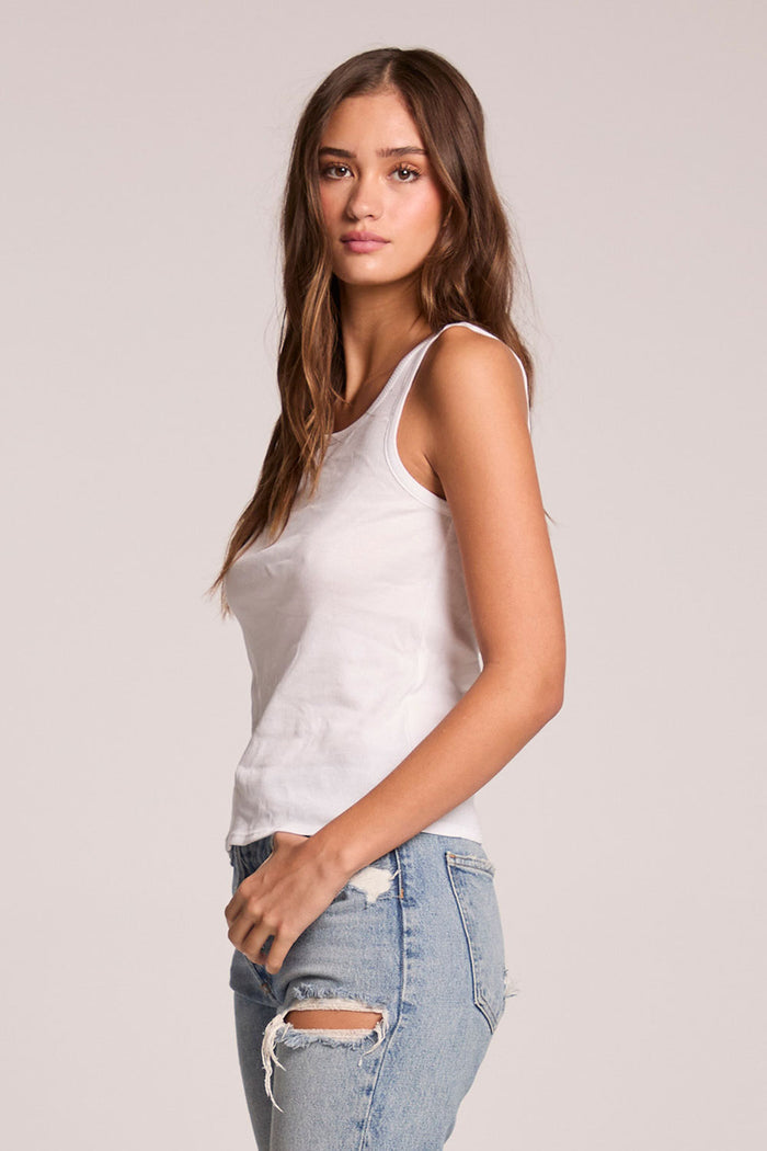 Side view of a woman wearing the Chaser    Daphne White Tank Top on a neutral background with hand on her pocket
