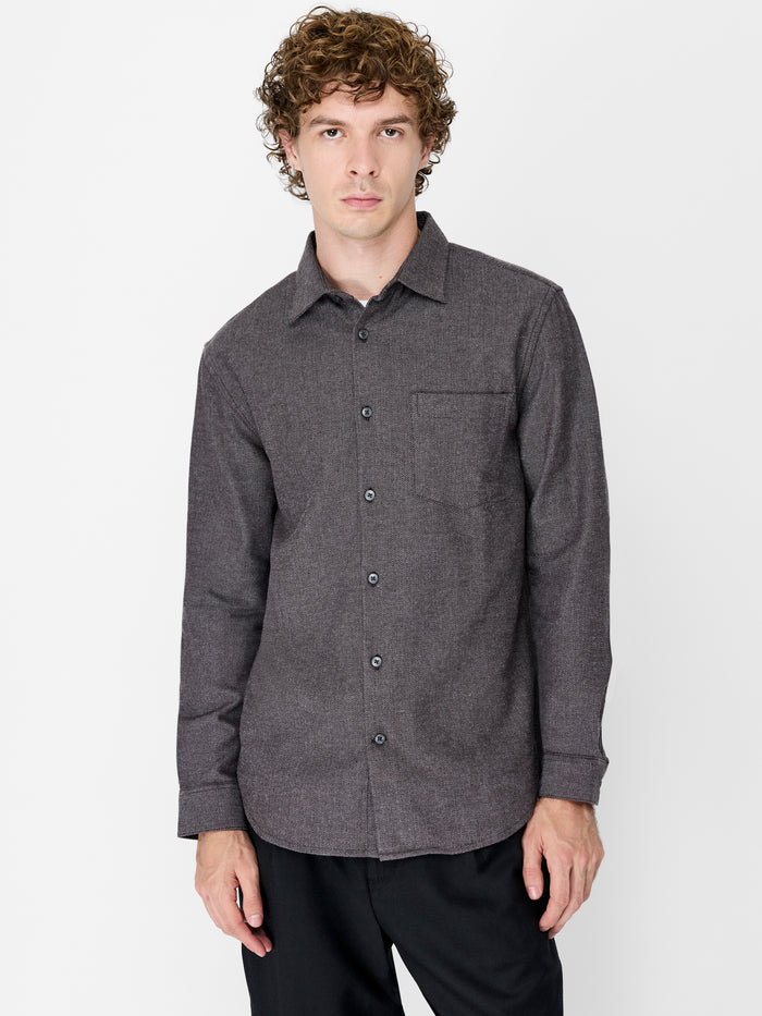 A man wearing a dark grey herringbone texture Shirt with long sleeves, a pointed collar, a chest pocket, a button through fastening and a regular fit.