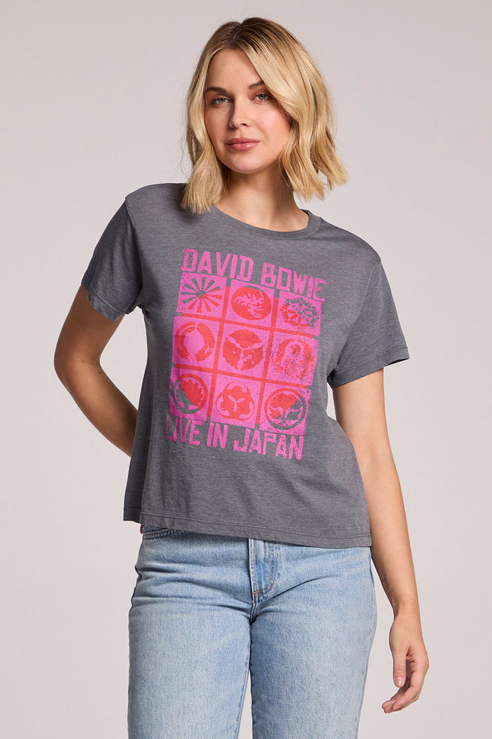 Front view of a woman wearing the Chaser David Bowie Live in Japan Tee with a hand on her hip on a neutral background