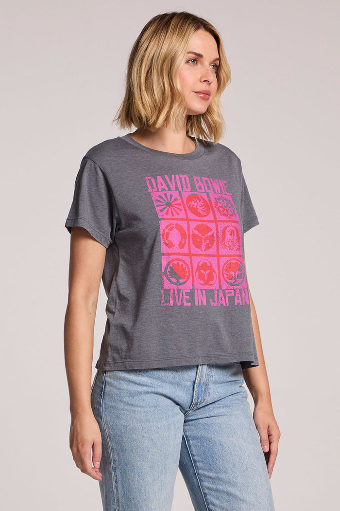 Side angle view of a woman wearing the Chaser David Bowie Live in Japan Tee with one leg extended on a neutral background