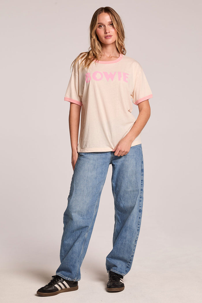 Front view of a woman wearing the Chaser  David Bowie Santa Monica '72 Tee and sneakers on a neutral background