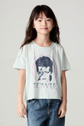 Side view of a girl wearing the Chaser David Bowie Stars Bowie Girls Tee on a neutral background with bluejeans and arms at her sides