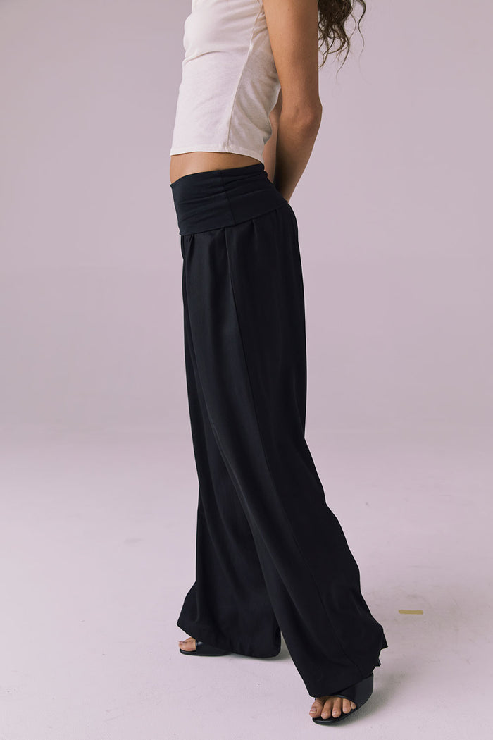 Side view of the Chaser Didion Licorice Black Trousers highlighting the relaxed wide leg and fluid movement with black heels