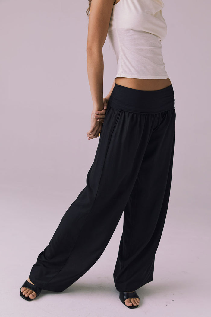 Model wearing the Chaser Didion Licorice Black Trousers leaning slightly forward to show the soft drape and foldover waistband
