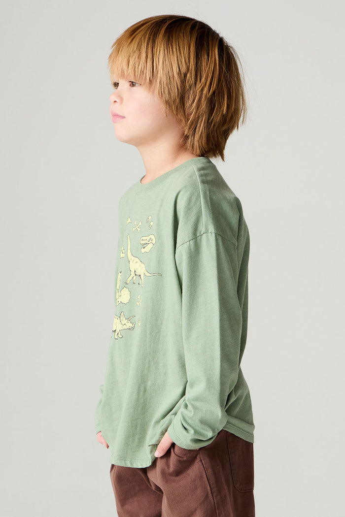 Side view of a boy wearing the Chaser Dino Action Boys Tee on a neutral background with hands in pockets of brown pants