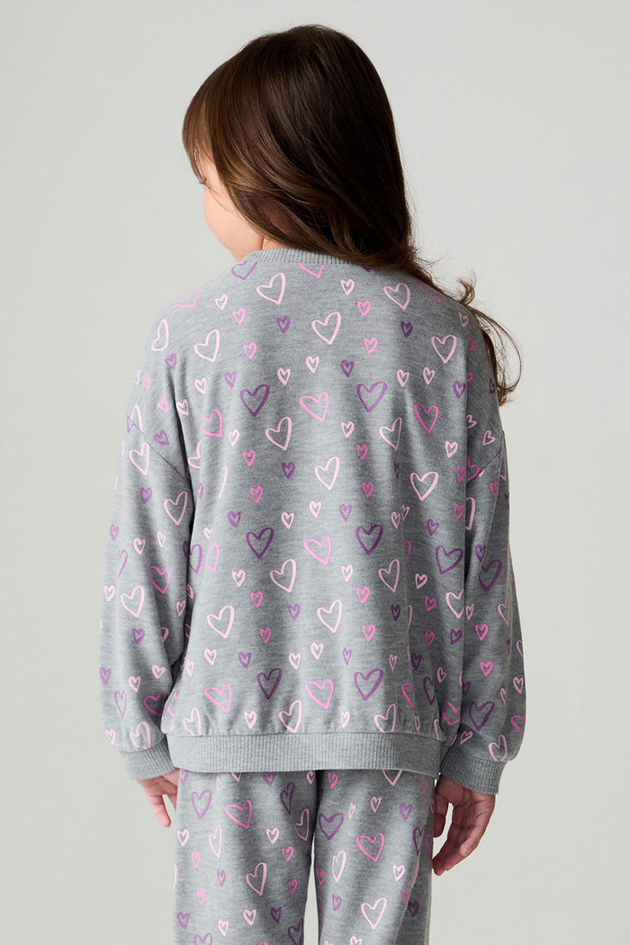Back view of a girl wearing the Chaser Ditsy Hearts Girls Tee and pants on a neutral background