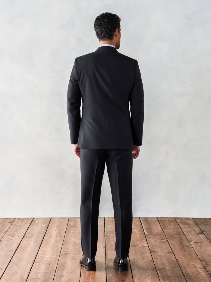 Back view of a man in a black double-breasted tuxedo, full length standing on a wood floor.
