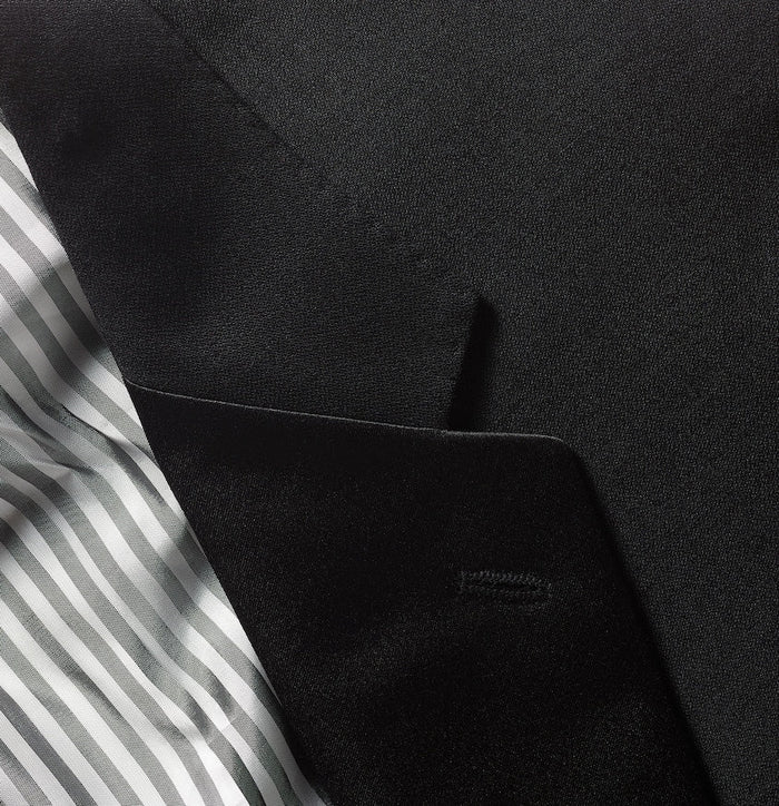 Close-up of black tuxedo jacket pocket and satin lapel edge against striped lining.