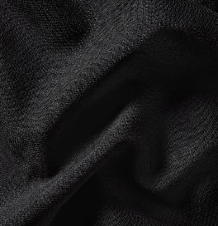 Close-up of black tuxedo trouser fabric showing soft folds and sheen.