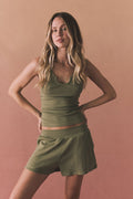 Editorial studio shot of the Chaser Durango Meadow Green Shorts shown with the matching Brandi Meadow Green Tank, styled against a warm blush backdrop for a relaxed yet polished look