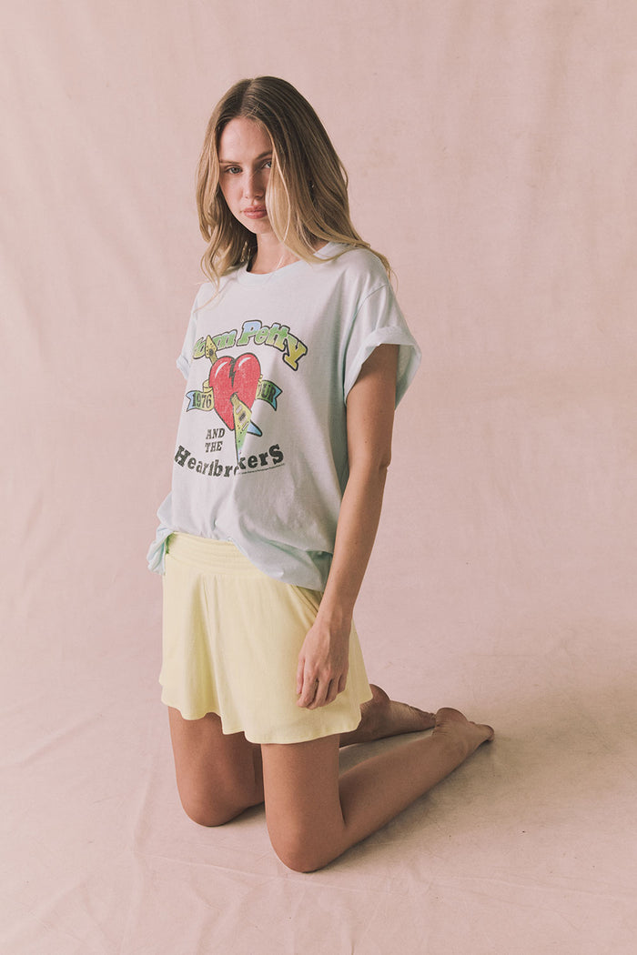 Model kneeling wearing Chaser Durango Shorts in Panna Cotta paired with Tom Petty 1976 Tour Tee licensed band collaboration on a plain background
