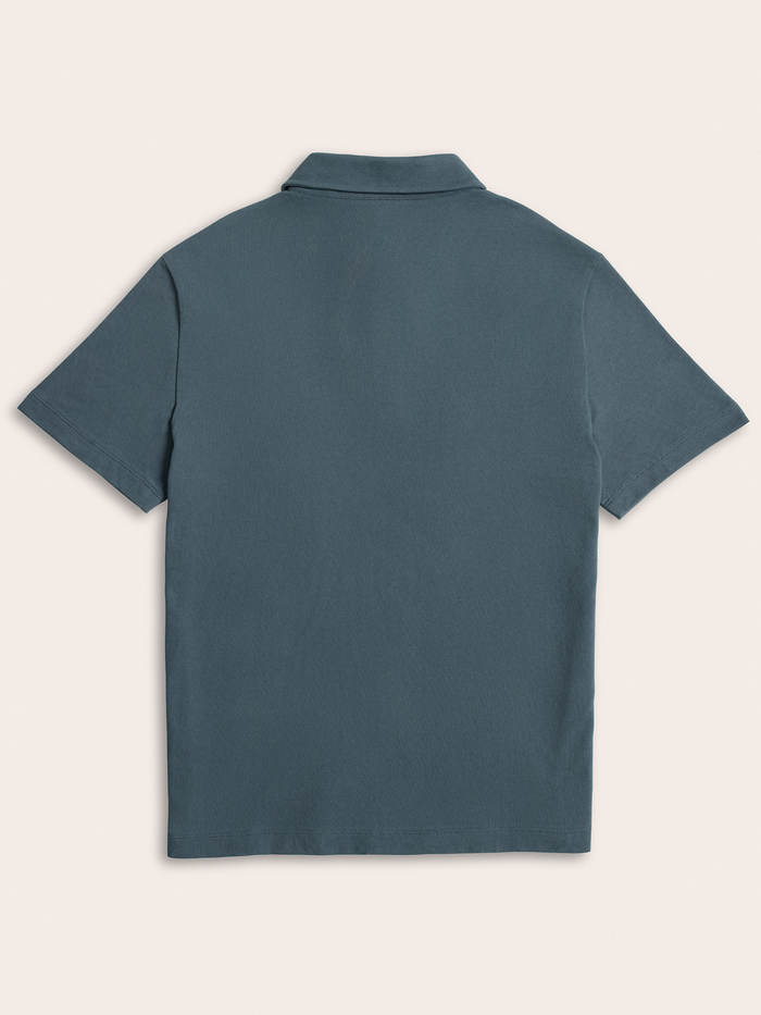 Slate blue pique polo shirt laid flat, back view, on cream background