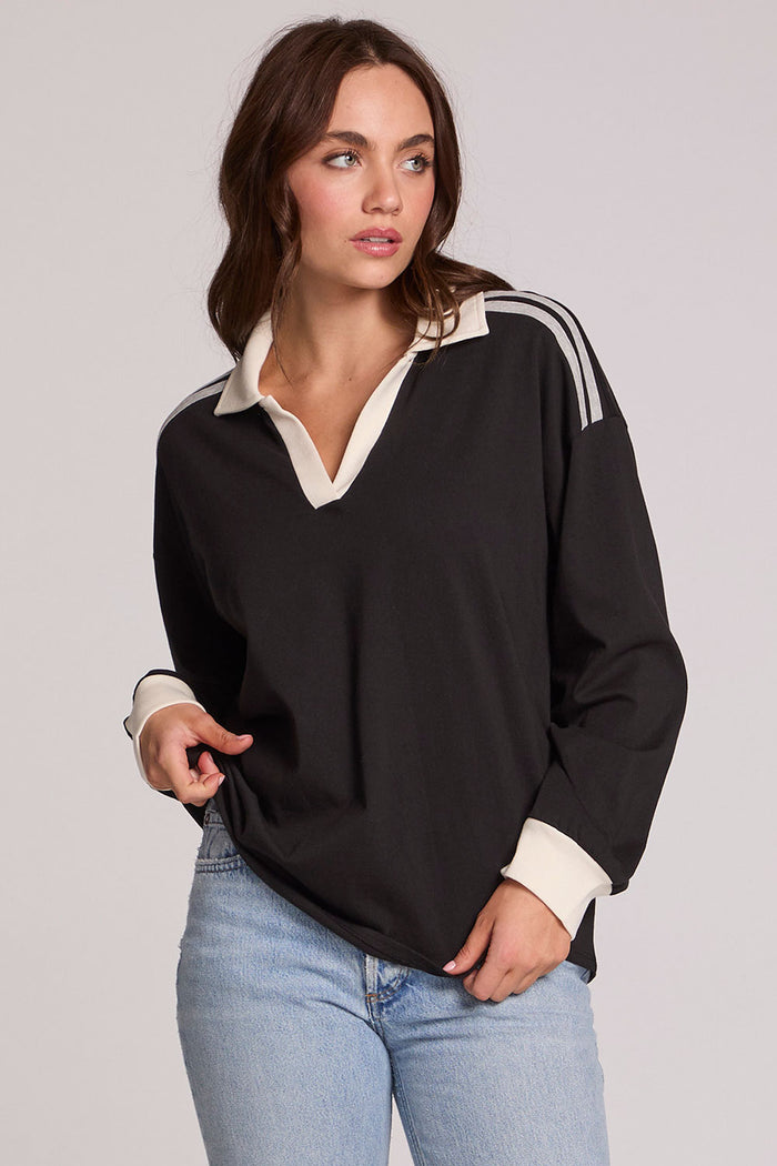 Front view of a woman wearing the Chaser Eddith Black and Heather Grey Collar Sweatshirt on a neutral background with bluejeans and hands on hem of shirt