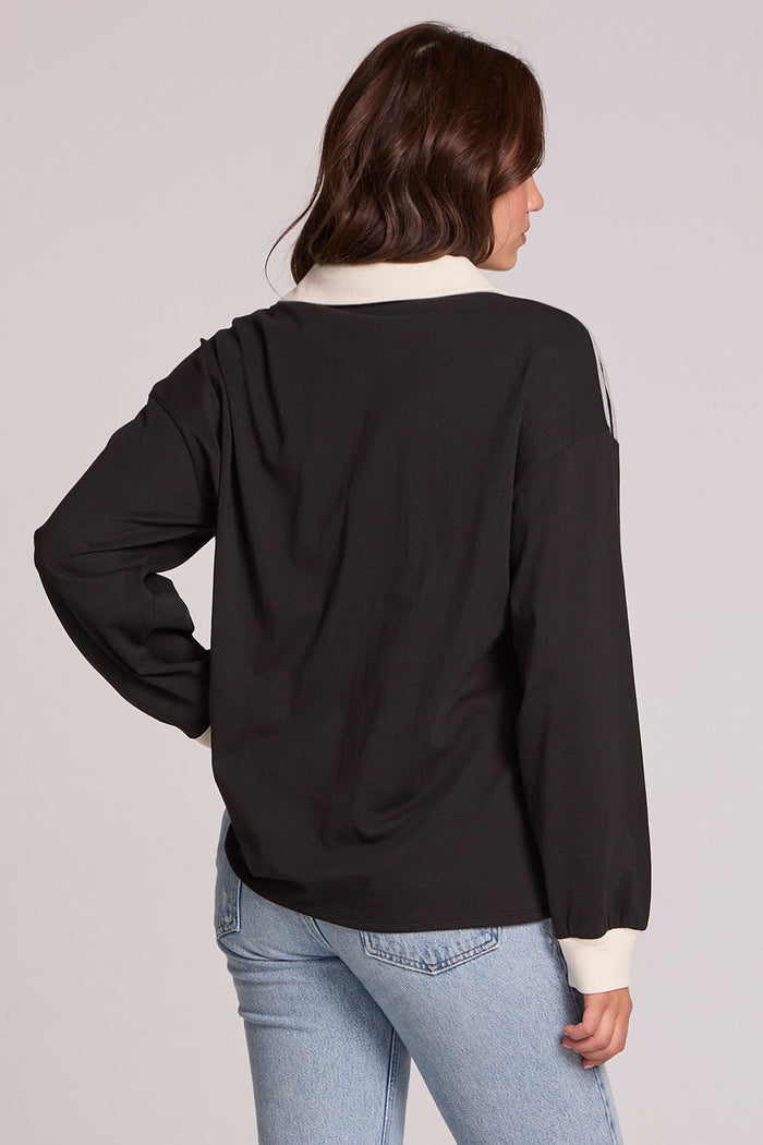 Back view of a woman wearing the Chaser Eddith Black and Heather Grey Collar Sweatshirt on a neutral background with jeans
