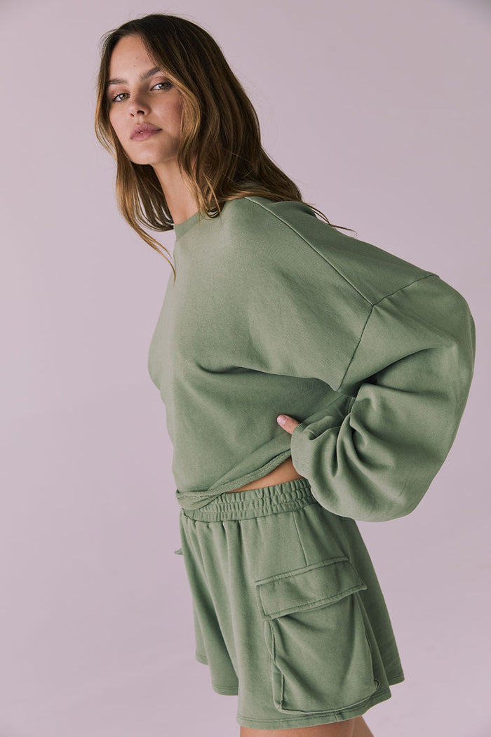 Three-quarter studio image of the Chaser Eliza Meadow Green Crop Pullover styled with Rileyy Shorts capturing the cozy silhouette and ribbed neckline