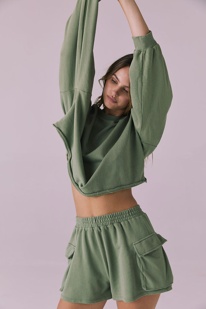 Studio shot of the Chaser Eliza Meadow Green Crop Pullover lifted slightly at the hem showing the elastic waistband of the matching Rileyy Shorts