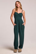 Front view of a woman wearing the Chaser  Ellery Pine Green Jumpsuit and clogs on a neutral background