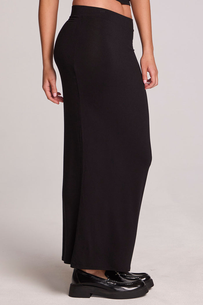 Side view of a woman wearing the Chaser  Eloyse Black Maxi Skirt and black shoes on a neutral background
