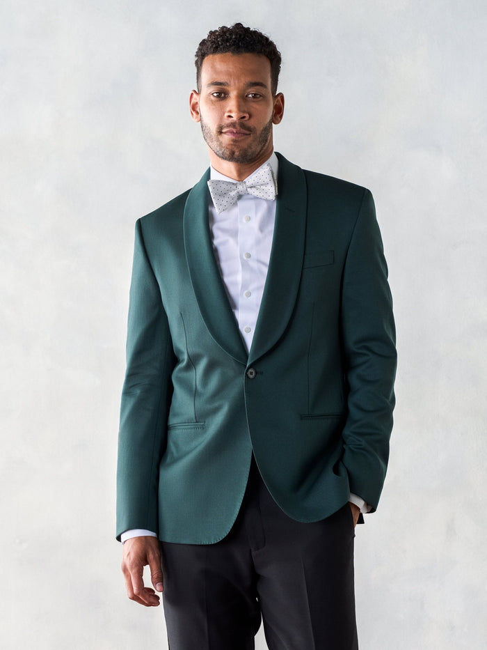 Man in an emerald green shawl-lapel tuxedo jacket with a patterned bow tie and black trousers.