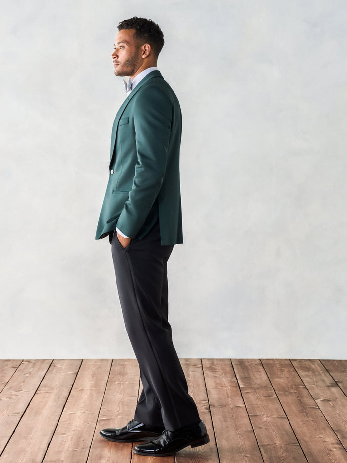 Side view of a man in an emerald green shawl-lapel tuxedo jacket and black trousers.