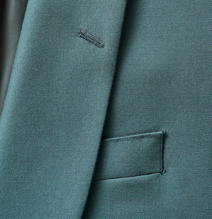 Close-up of emerald green tuxedo jacket lapel and welt pocket detail.