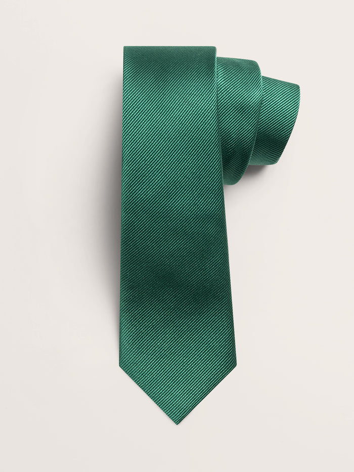 Emerald green silk necktie rolled into a loose coil on a cream background.