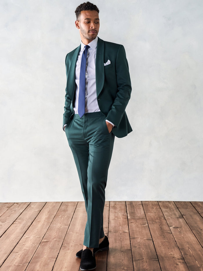 Man walking in an emerald green suit with a navy tie and white pocket square.
