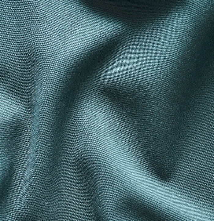 Close-up of emerald green tuxedo trouser fabric showing soft folds and sheen.
