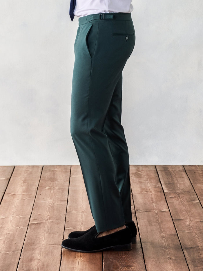 Side view of a man from waist down in emerald green trousers, on a wood floor.